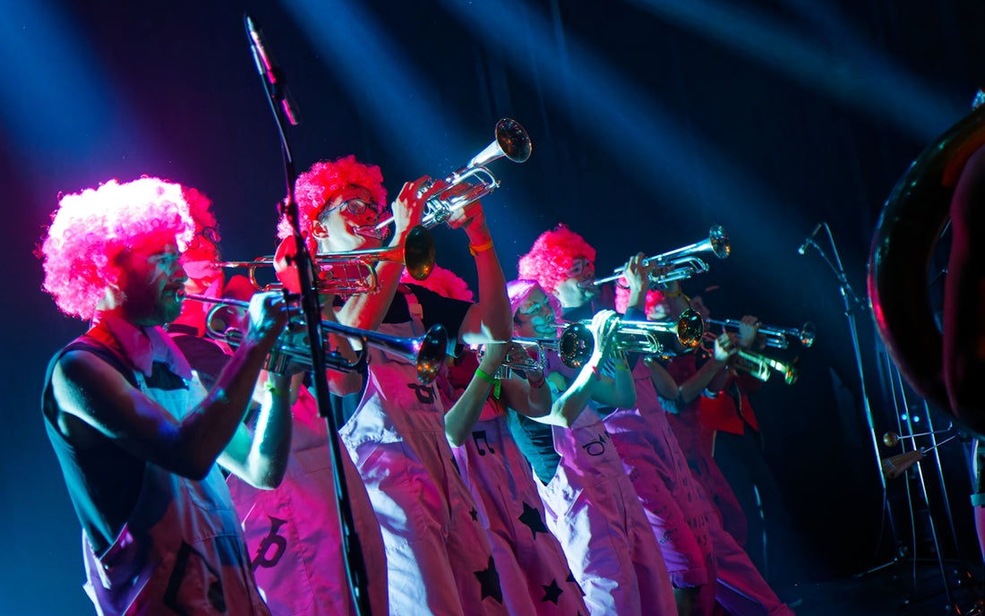 Musicians in pink wigs play trumpets on stage