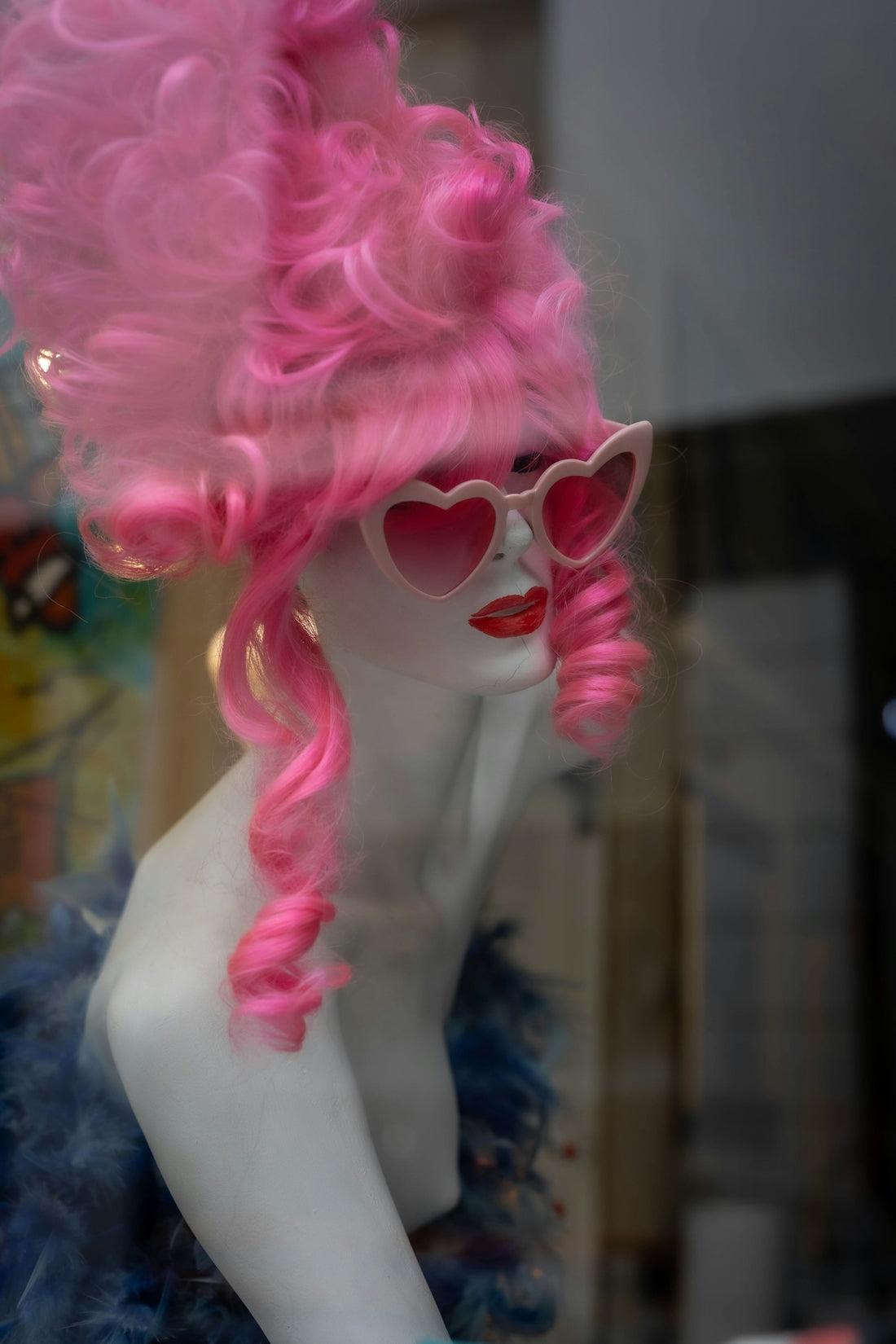 Mannequin in pink wig, heart sunglasses, and blue feather boa.