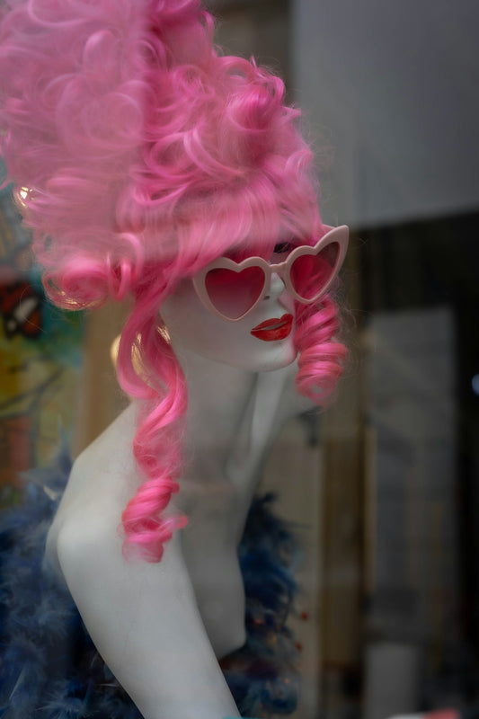 Mannequin in pink wig, heart sunglasses, and blue feather boa.