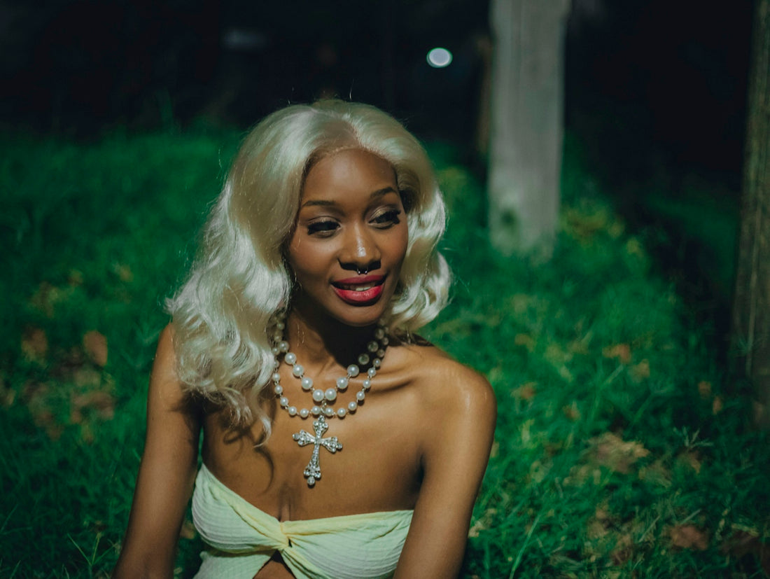 Blonde woman with pearl necklace sitting on green grass