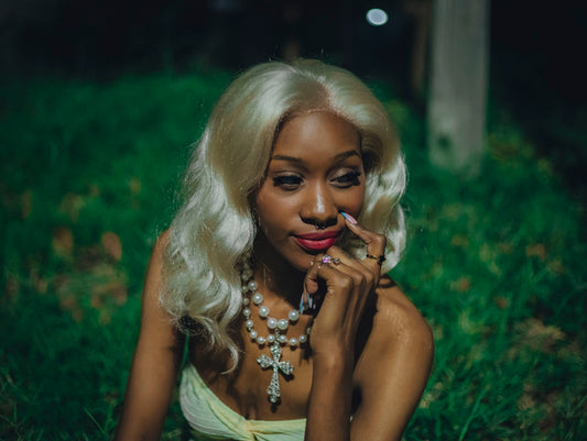 Blonde woman wearing a pearl cross necklace in dark grass.