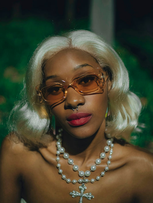 A young woman with blonde hair, sunglasses, and pearl necklaces.
