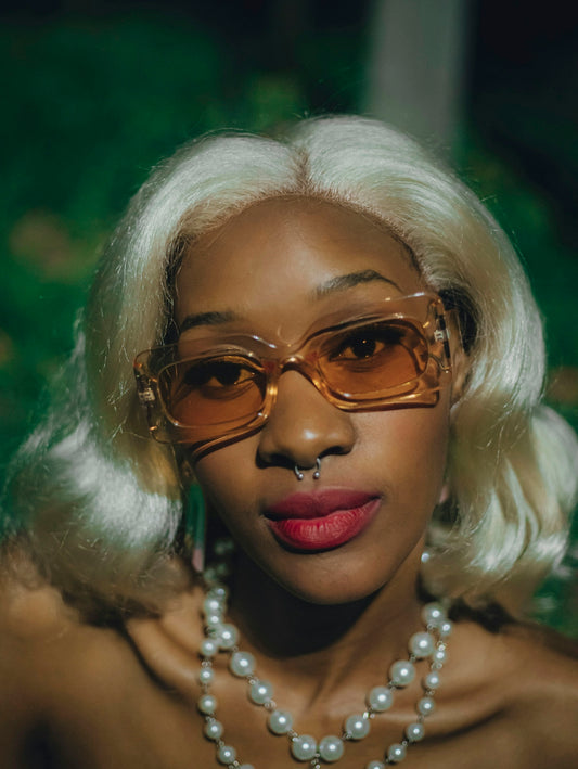 Blonde woman with sunglasses, nose ring, and pearl necklace.